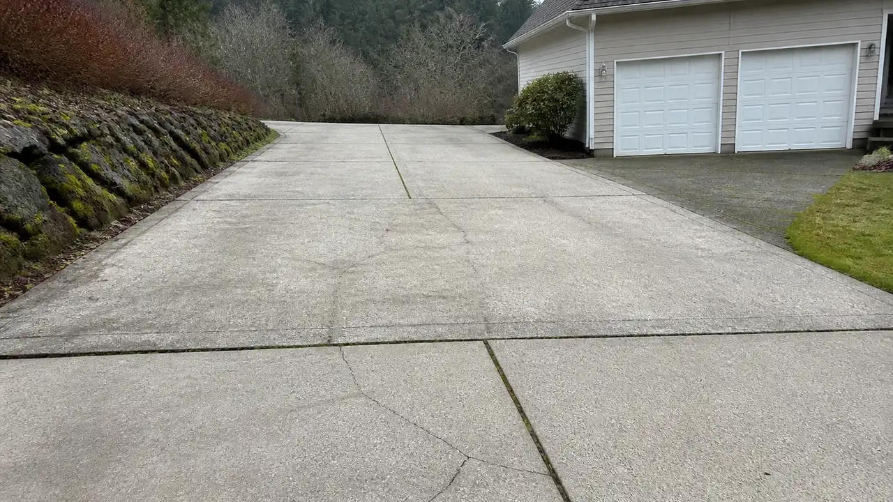 Illustrative view of a concrete driveway with a cracked panel in an Issaquah-style foothill residential setting.